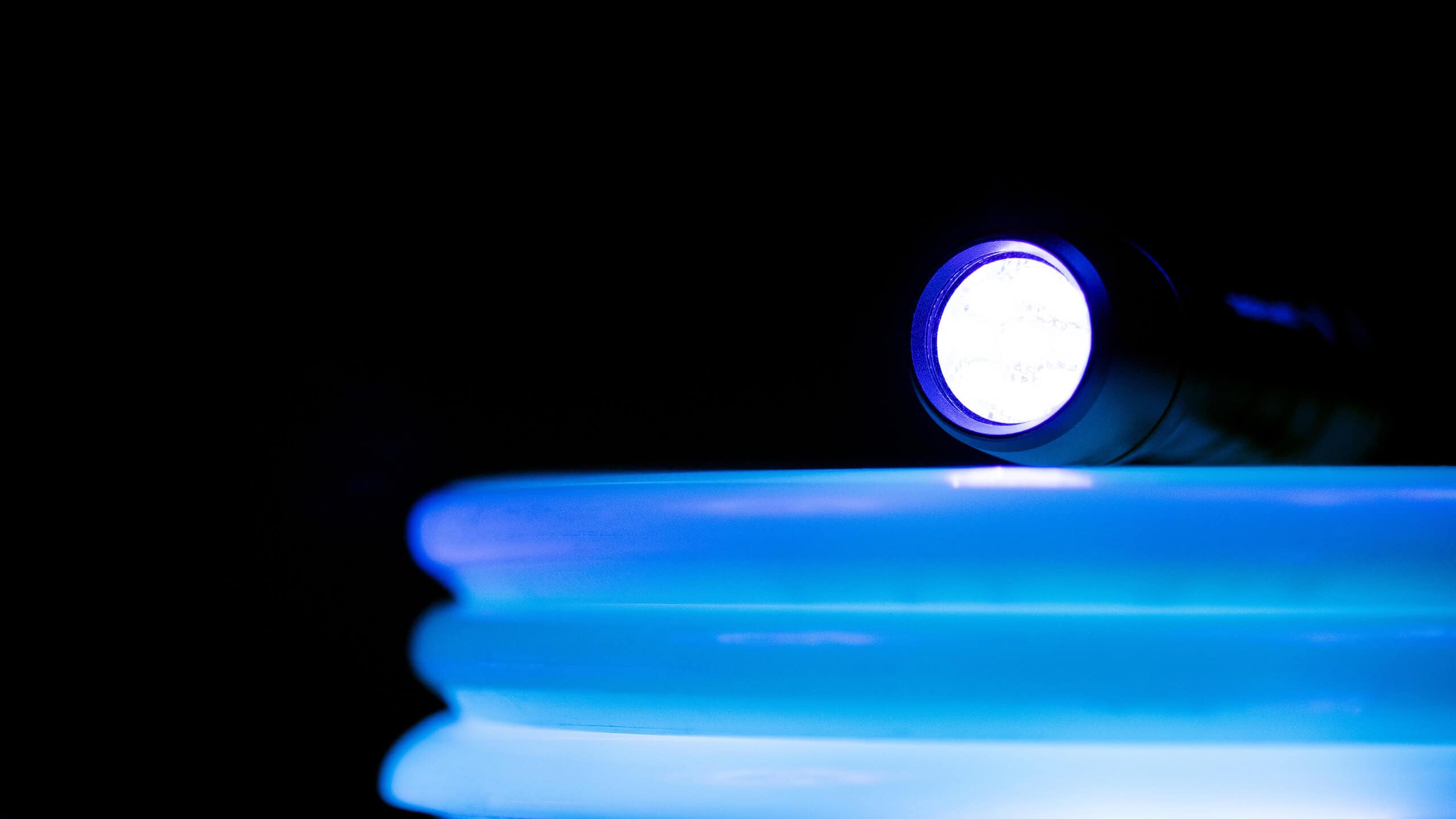 A stack of ultraviolet glow in the dark flying discs used for disc golf with UV flashlight.
